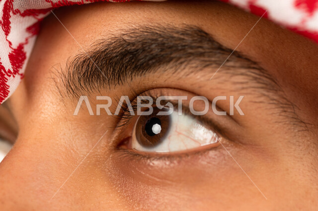 Close-up portrait of a Saudi Gulf man doing a photo session, looking up, white background of a Saudi Muslim man wearing traditional Saudi dress with shemagh and headband