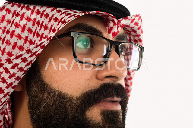 بورتريه بصورة مقربة لرجل سعودي خليجي يقوم بجلسة تصوير ، ينظر لأعلى ، خلفية بيضاء لرجل سعودي مسلم يرتدي زي تقليدي سعودي مع شماغ وعقال