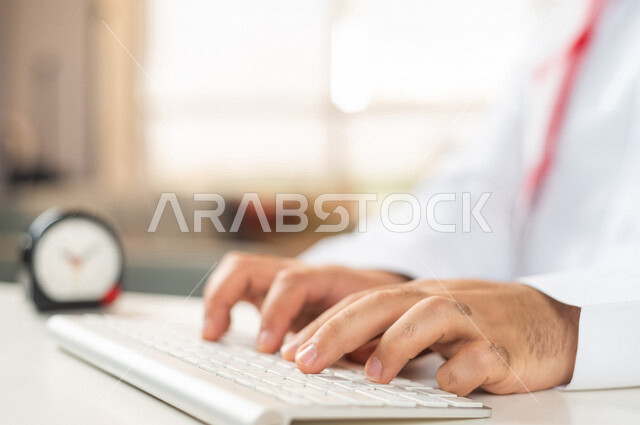 صورة مقربة لرجل أعمال سعودي خليجي ، استخدام لوحة المفاتيح للكتابة ، ساعة رقمية صغيرة على الطاولة ، مفهوم إدارة وقت العمل ، الدقة في المواعيد ، التذكيرات والتنبيهات ، العمل عن بعد ، التسويق الإلكتروني ، إنجاز المهامات في الوقت
