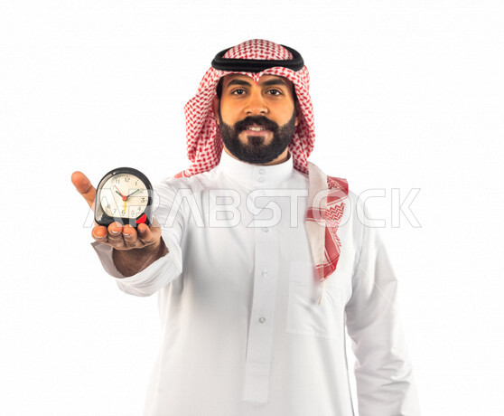 بورتريه لرجل سعودي خليجي يحمل ساعة رقمية صغيرة بإيماءات وجه ويدين مختلفة ، خلفية بيضاء لرجل سعودي يرتدي الزي التقليدي السعودي مع شماغ وعقال ، مفهوم إدارة وقت العمل ، الدقة في المواعيد ، التذكيرات والتنبيهات الثابته ، مواعيد العمل ، إنجاز المهامات في الوقت