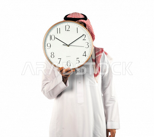 بورتريه لرجل سعودي خليجي يحمل ساعة رقمية كبيرة بإيماءات وجه ويدين مختلفة ، خلفية بيضاء لرجل سعودي يرتدي الزي التقليدي السعودي مع شماغ وعقال ، مفهوم العد التنازلي ، الدقة في المواعيد ، التذكيرات والتنبيهات الثابته ، مواعيد العمل ، إنجاز المهامات في الوقت