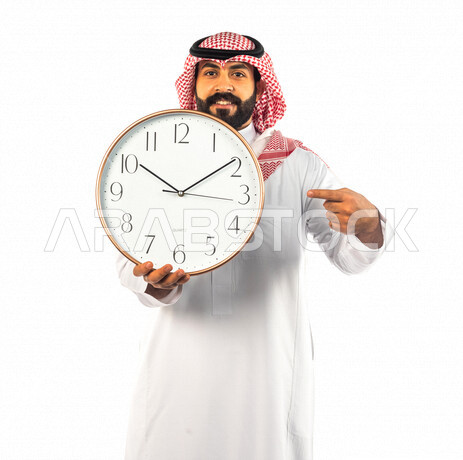 بورتريه لرجل سعودي خليجي يحمل ساعة رقمية كبيرة بإيماءات وجه ويدين مختلفة ، خلفية بيضاء لرجل سعودي يرتدي الزي التقليدي السعودي مع شماغ وعقال ، مفهوم العد التنازلي ، الدقة في المواعيد ، التذكيرات والتنبيهات الثابته ، مواعيد العمل ، إنجاز المهامات في الوقت