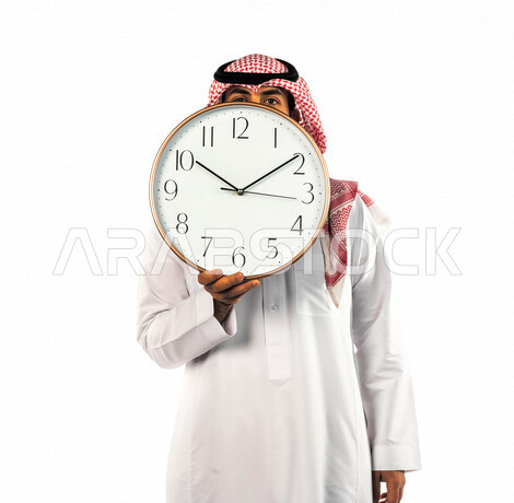 بورتريه لرجل سعودي خليجي يحمل ساعة رقمية كبيرة بإيماءات وجه ويدين مختلفة ، خلفية بيضاء لرجل سعودي يرتدي الزي التقليدي السعودي مع شماغ وعقال ، مفهوم العد التنازلي ، الدقة في المواعيد ، التذكيرات والتنبيهات الثابته ، مواعيد العمل ، إنجاز المهامات في الوقت
