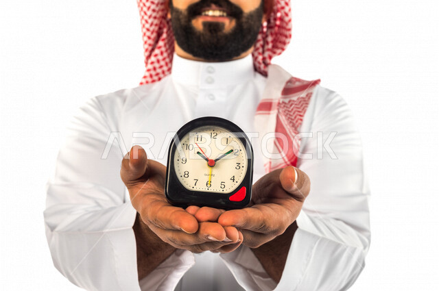 بورتريه لرجل سعودي خليجي يحمل ساعة رقمية صغيرة بإيماءات وجه ويدين مختلفة ، خلفية بيضاء لرجل سعودي يرتدي الزي التقليدي السعودي مع شماغ وعقال ، مفهوم إدارة وقت العمل ، الدقة في المواعيد ، التذكيرات والتنبيهات الثابته ، مواعيد العمل ، إنجاز المهامات في الوقت