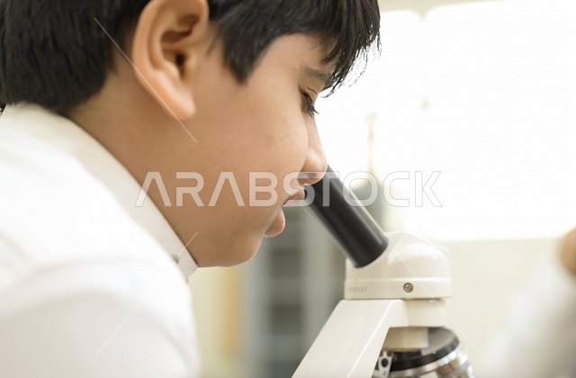 تلميذ عربي خليجي سعودي يرتدي الزي المدرسي، اجراء البحوثات والاختبارات باستخدم التلسكوب داخل مختبر المدرسة، بحوث علمية، التعليم في المملكة العربية السعودية