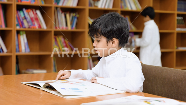 A picture of a Saudi Arabian Gulf student sitting in the school library, enjoying reading the textbook, school library, education in Saudi Arabia