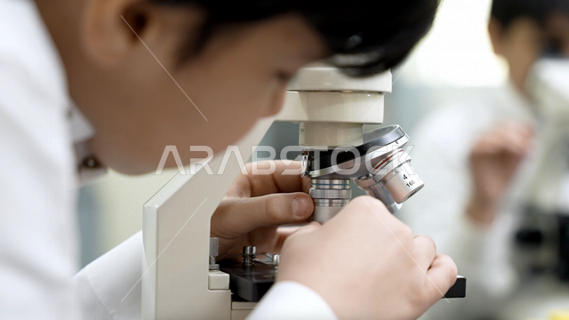 تلميذ عربي خليجي سعودي يرتدي الزي المدرسي، اجراء البحوثات والاختبارات باستخدم التلسكوب داخل مختبر المدرسة، بحوث علمية، التعليم في المملكة العربية السعودية