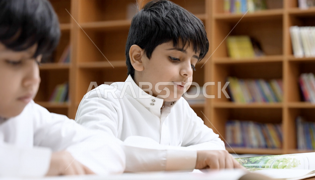 طالبان عربيان سعوديان خليجيان في المكتبة المدرسية، الاستمتاع بقراءة الكتب المدرسية، مكتبة المدرسة، تأدية الواجبات المدرسية، التعليم في المملكة العربية السعودية