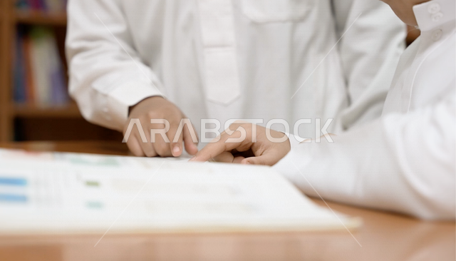 طالبان عربيان سعوديان خليجيان في المكتبة المدرسية، الاستمتاع بقراءة الكتب المدرسية، مكتبة المدرسة، تأدية الواجبات المدرسية، التعليم في المملكة العربية السعودية