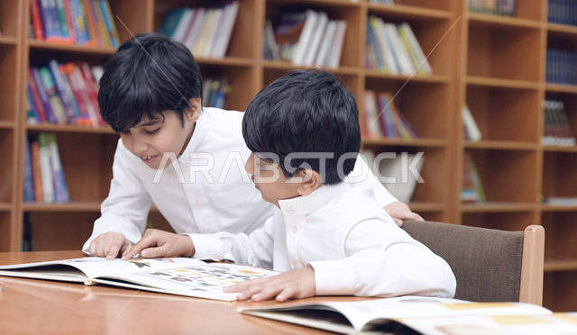 طالبان عربيان سعوديان خليجيان في المكتبة المدرسية، الاستمتاع بقراءة الكتب المدرسية، مكتبة المدرسة، تأدية الواجبات المدرسية، التعليم في المملكة العربية السعودية