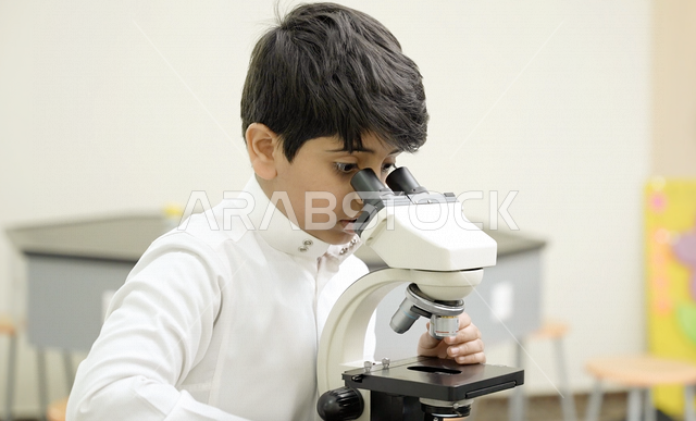 تلميذ عربي خليجي سعودي يرتدي الزي المدرسي، اجراء البحوثات والاختبارات باستخدم التلسكوب داخل مختبر المدرسة، بحوث علمية، التعليم في المملكة العربية السعودية