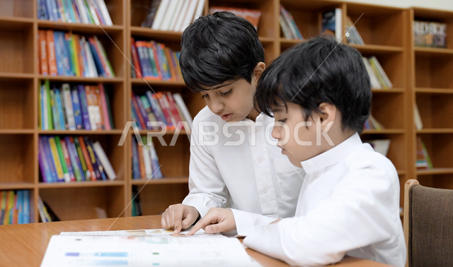 طالبان عربيان سعوديان خليجيان في المكتبة المدرسية، الاستمتاع بقراءة الكتب المدرسية، مكتبة المدرسة، تأدية الواجبات المدرسية، التعليم في المملكة العربية السعودية