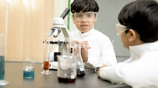 تلميذان عربيان خليجيان سعوديان يرتديان الزي المدرسي، اجراء البحوثات والاختبارات باستخدم التلسكوب داخل مختبر المدرسة، بحوث علمية، تسجيل الملاحظات، التعليم في المملكة العربية السعودية