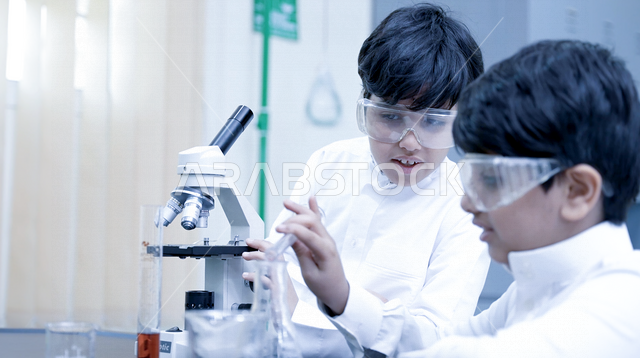 تلميذان عربيان خليجيان سعوديان يرتديان الزي المدرسي، اجراء البحوثات والاختبارات باستخدم التلسكوب داخل مختبر المدرسة، بحوث علمية، تسجيل الملاحظات، التعليم في المملكة العربية السعودية