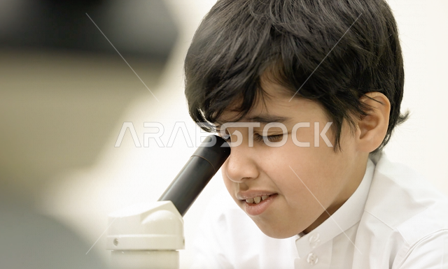 تلميذ عربي خليجي سعودي يرتدي الزي المدرسي، اجراء البحوثات والاختبارات باستخدم التلسكوب داخل مختبر المدرسة، بحوث علمية، التعليم في المملكة العربية السعودية