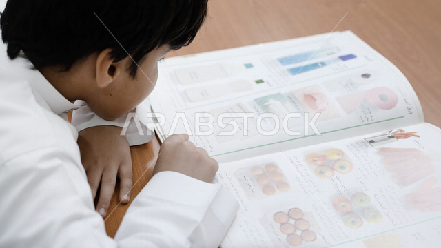 صورة مقربة لتلميذ عرب خليجي سعودي يجلس في المكتبة المدرسية، الاستمتاع بقراءة الكتاب المدرسي، مكتبة المدرسة، التعليم في المملكة العربية السعودية