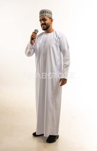 إلقاء المحاضرات وإقامة الندوات, ممارسة موهبة الغناء, العمل في تقديم الفقرات و البرامج الفنية الترفيهية, إيماءات السعادة و الاستمتاع, بورتريه لشاب عربي خليجي عماني يرتدي الدشداشة و الكمة يمسك بيده المايكروفون، الجسم بالطول الكامل, خلفية بيضاء