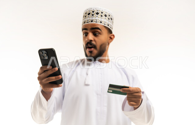 التقنيات الحديثة المتطورة، استخدام تطبيقات الجوال للدفع والشراء، إمكانية تسديد الفواتير عبر بطاقة الصراف, بورتريه مقرب لشاب عربي خليجي عماني مبتسم يرتدي الدشداشة و الكمة يمسك بيده البطاقة الالكترونية ينظر الى الكاميرا بإيماءات السرور, خلفية بيضاء