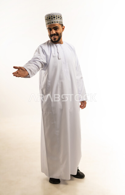 استخدام حاسة اللمس لتحريك العناصر الهولوجراميه، حمل ورفع شيء ما، بورتريه لشاب عربي خليجي عماني مبتسم يرتدي الدشداشة و الكمه يرفع يده للاعلى بإيماءات الترحيب، النظر الى الكاميرا بتعابير السرور، الإشارة نحو هدف معين، صورة الجسم بالطول الكامل، خلفية بيضاء
