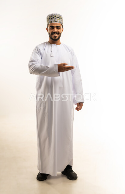 حمل ورفع شيء ما، استخدام حاسة اللمس لتحريك العناصر الهولوجراميه، بورتريه لشاب عربي خليجي عماني مبتسم يرتدي الدشداشة و الكمه يرفع يده للاعلى بإيماءات الترحيب، النظر الى الكاميرا بتعابير السرور، الإشارة نحو هدف معين، صورة الجسم بالطول الكامل، خلفية بيضاء