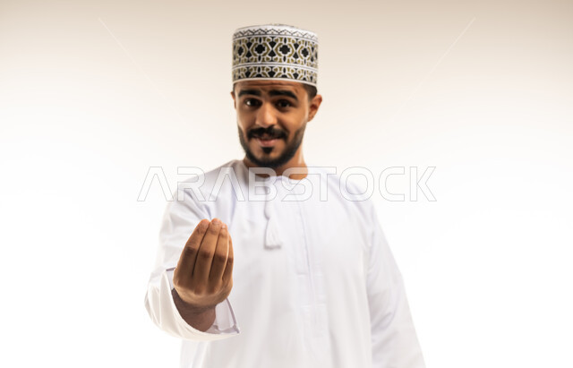 مفهوم الصبر والتريث، إمهال بعض الوقت للقيام بشئ ما، بورتريه مقرب لرجل عربي خليجي عماني يرتدي الدشداشة والكمه ينظر الى الكاميرا يشير بيده بإيماءات طلب الإنتظار، مفهوم الصبر والتأن والتريث، خلفية بيضاء