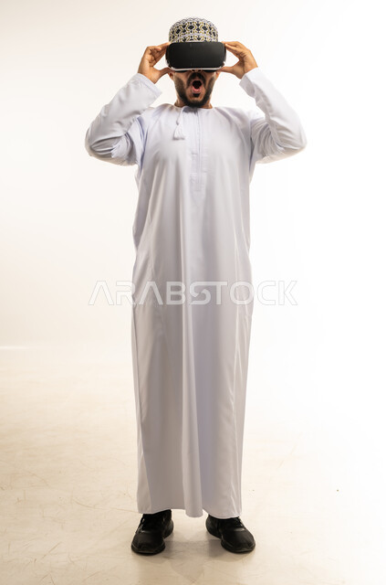 التطور التقني والتكنولوجي, المتعة و التسلية بالمشاهدة عبر نظارة الواقع الافتراضي، بورتريه لشاب عربي خليجي عماني يرتدي الدشداشة والكمه ينظر من خلال نظارات ثلاثية الأبعاد (الفي ار), الاندماج ومحاكاة العالم الخيالي، صورة الجسم بالكامل، خلفية بيضاء