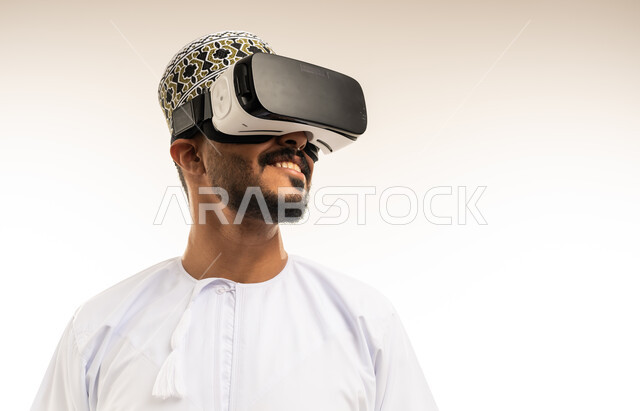 التسلية والمتعة بالمشاهدة عبر نظارة الواقع الافتراضي، التطور التقني والتكنولوجي, بورتريه مقرب لشاب عربي خليجي عماني يرتدي الدشداشة والكمه ينظر من خلال نظارات ثلاثية الأبعاد (الفي ار), الاندماج ومحاكاة العالم الخيالي، خلفية بيضاء