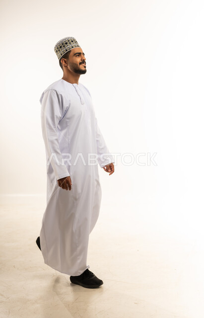 Concern for elegance and appearance, portrait of a smiling young Omani Gulf Arab man wearing a dishdasha and a turban, looking forward and walking quickly, the concept of masculinity and self-confidence, full-length body image, white background