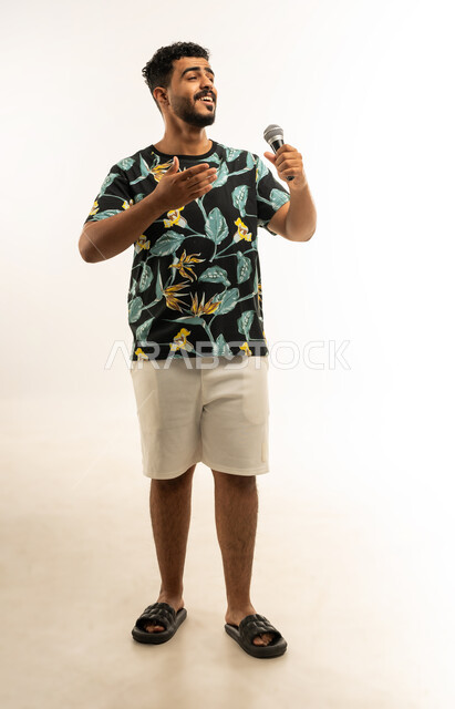 تقديم العروض الصوتية، تسجيل مقطع صوتي غنائي، تعابير الاندماج والتفاعل مع الموسيقا، بورتريه لشاب عربي خليجي عماني مبتسم يرتدي الزي الكاجوال يمسك بيده المايكروفون يقوم بالغناء بإيماءات الفرح والسرور، صورة الجسم بالطول الكامل، خلفية بيضاء