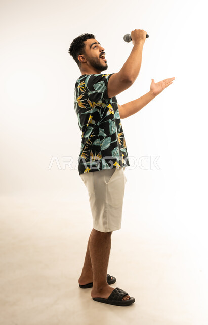 Recording a singing audio clip, expressions of integration and interaction with music, close-up portrait of a smiling young Arab Gulf Omani man in casual clothes holding a microphone in his hand singing with gestures of joy and happiness, vocal performance, full-length body image, white background