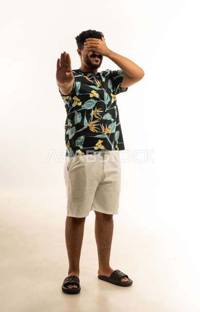 الإمتناع عن فعل شيء ما، تعابير وإشارات لطلب التوقف و عدم الاقتراب، بورتريه لشاب عربي خليجي عماني يرتدي الزي الكاجوال يرفع كفه للأعلى يضع يده على عينيه بإيماءات الخوف والذعر والصدمة، صورة الجسم بالطول الكامل، خلفية بيضاء