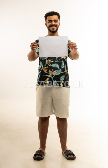White square mockup, using informative illustrations, portrait of a smiling young Arab Gulf Omani man in casual clothes holding a blank square white board in his hand looking at the camera with gestures of joy and happiness, advertisements and marketing offers, full body image, white background