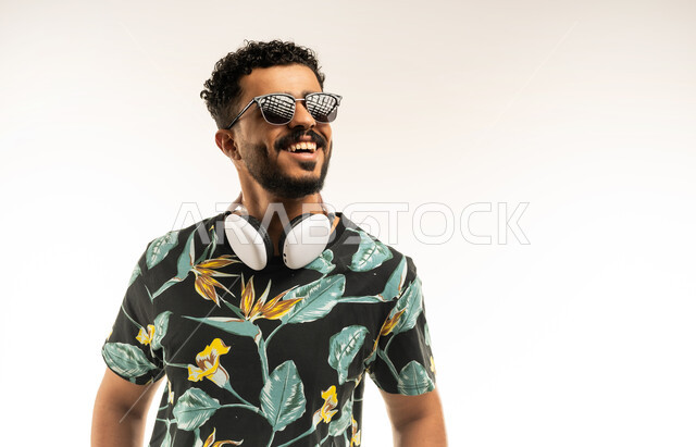قضاء رحلة صيفية ممتعة, الاستعداد للذهاب في جولات ترفيهية في إجازة الصيف, تعابير الفرح والسرور، بورتريه مقرب لشاب عربي خليجي عماني مبتسم يرتدي الزي الكاجوال والنظارة الشمسية ينظر الى شيء ما بإيماءات السعادة, صورة الجسم بالطول الكامل، خلفية بيضاء