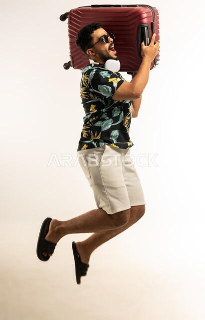 الذهاب في جولات ترفيهية في إجازة الصيف, تعابير الفرح والسرور، بورتريه  لشاب عربي خليجي عماني مبتسم يرتدي الزي الكاجوال والنظارة الشمسية يحمل حقيبة السفر على كتفه, الاستعداد لقضاء رحلة صيفية ممتعة, صورة الجسم بالطول الكامل، خلفية بيضاء