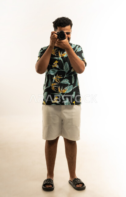 Mastering and professionalizing the photography profession, portrait of a smiling young Arab Gulf Omani man wearing casual clothes taking souvenir photos with a camera, expressions of joy and happiness, using high-resolution digital cameras, full-length body photo, white background