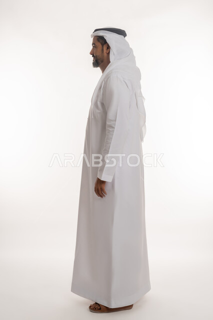 الأناقة والاهتمام بالمظهر الخارجي, مفهوم الرجولة والثقة بالنفس, بورتريه من الجانب لرجل عربي خليجي إماراتي يرتدي الكندورة والغترة يقف باستعداد واستقامة بتعابير السرور، صورة الجسم بالطول الكامل, خلفية بيضاء