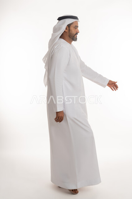 مفهوم الاهتمام بالمظهر الخارجي والاناقه، الوقوف باستقامه بتعابير الثقه بالنفس، بورتريه من الجانب لرجل عربي خليجي اماراتي يرتدي الكندوره والغتره البيضاء يقف بايماءات الرجولة، الجسم بالطول الكامل، خلفية بيضاء