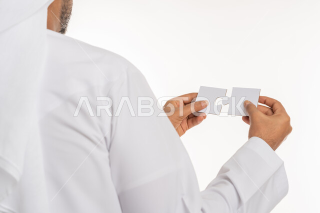 Entertainment and fun, intelligence and skill development games, accuracy, focus and puzzle solving, close-up portrait from behind of the hand of an Arab Gulf Emirati man wearing a kandura holding two pieces of a puzzle, jigsaw puzzle game, white background