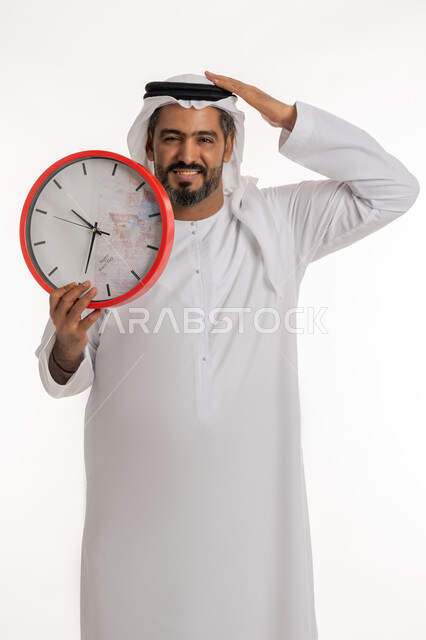 انجاز المهامات في الوقت، بورتريه لرجل عربي خليجي اماراتي مبتسم يرتدي الكندورة والغترة الاماراتية يحمل بيده ساعة رقمية كبيرة يضع يده على رأسه،  النظر الى الكاميرا بتعابير الفرح والسرور، الدقة في المواعيد ، التذكيرات والتنبيهات الثابته، مفهوم العد التنازلي، خلفية بيضاء