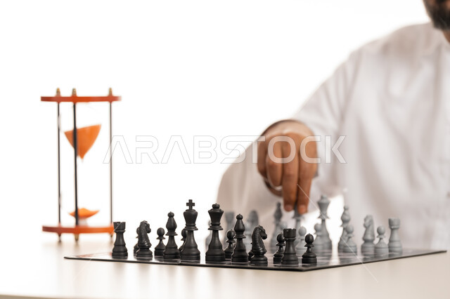 التسلية والترفيه وقضاء وقت ممتع، مفهوم التخطيط والتفكير في استراتيجية مناسبة, بورتريه مقرب لرجل عربي خليجي اماراتي يرتدي الكندورة يقوم بتحريك الحجر في لعبة الشطرنج, ألعاب الذكاء والتركيز والتحدي، تحقيق الفوز والانتصار بوقت زمني محدد, خلفية بيضاء