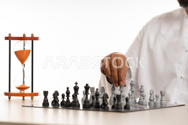 Entertainment, fun and having a good time, the concept of planning and thinking about a suitable strategy, a close-up portrait of an Arab Gulf Emirati man wearing a kandura moving a stone in a chess game, games of intelligence, focus and challenge, achieving victory and triumph within a specific time, white background