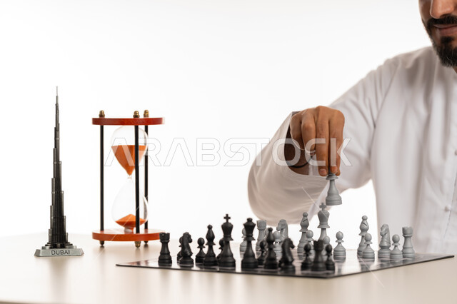 The concept of planning and thinking about a suitable strategy, a close-up portrait of an Arab Gulf Emirati man wearing a kandura moving a stone in a chess game, entertainment, amusement and spending a good time, games of intelligence, focus and challenge, achieving victory and triumph within a specific time, white background