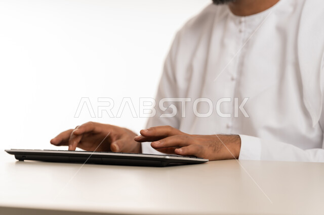 Office jobs and professions, use of modern technology and devices, close-up portrait of the hands of an Emirati Gulf Arab man wearing a kandura typing on a keyboard, integrating work with technology and technology in the United Arab Emirates