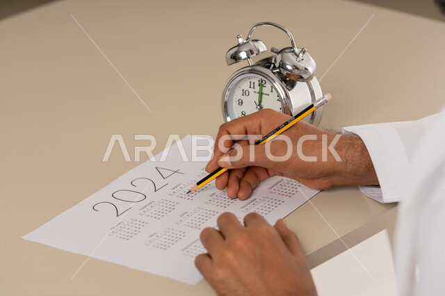 انجاز المهام بالموعد المحدد, أهمية تنظيم الوقت, إدارة وتحديد وقت العمل, صورة مقربة ليد رجل عربي خليجي اماراتي يقوم بتسجيل المواعيد على جدول التقويم الزمني, مفهوم التذكير والتنبيه