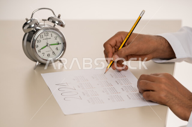 أهمية تنظيم الوقت, إدارة وتحديد وقت العمل, بورتريه مقرب ليد رجل عربي خليجي اماراتي يقوم بتسجيل المواعيد على جدول التقويم الزمني, مفهوم التذكير والتنبيه, انجاز المهام بموعد محدد, خلفية بيضاء