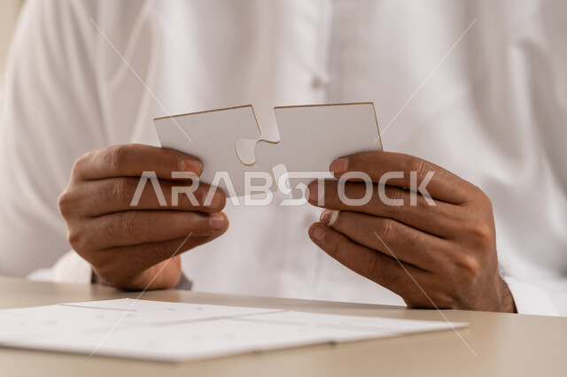 التسلية والترفيه وقضاء الوقت الممتع, ألعاب الذكاء وتنمية المهارات, الدقة والتركيز وحل اللغز, صورة مقربة ليد رجل عربي خليجي اماراتي يرتدي الكندورة يحاول ربط وتوصيل قطع البزل, لعبة تركيب الصور