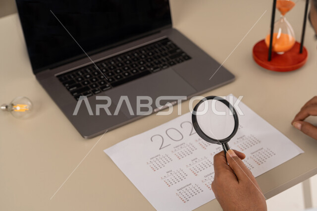 Concept of image clarification, use of modern and advanced devices and technologies, close-up image of the hand of an Arab Gulf Emirati man holding a magnifying glass, concept of examination and exploration, close-up view of the calendar, concept of schedule management, setting work schedules