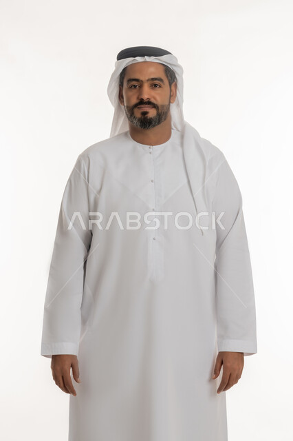 Elegance and interest in appearance, concept of masculinity and self-confidence, portrait of an Arab Gulf Emirati man wearing a kandura and a ghutra looking at the camera with an expression of pleasure, standing ready and straight, white background