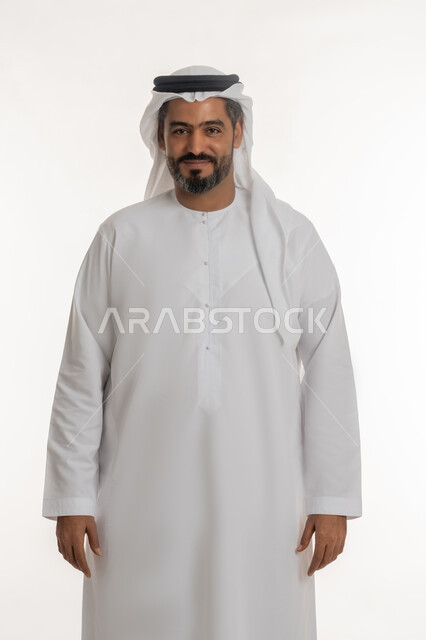 مفهوم الرجولة والثقة بالنفس, بورتريه لرجل عربي خليجي إماراتي يرتدي الكندورة والغترة ينظر الى الكاميرا بتعابير السرور، الوقوف باستعداد واستقامة، الأناقة والاهتمام بالمظهر الخارجي، خلفية بيضاء