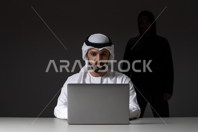 التسلل عبر الأمن السيبراني, قرصنة وسرقة البيانات, التعرض للهجمات والاختراقات، اختراق حماية وأمن وخصوصية المستخدمين, بورتريه لرجل عربي خليجي إماراتي يرتدي الكندورة والغترة البيضاء يستخدم جهاز الحاسوب المحمول ويقف ورائه المخترق, خلفية رمادية